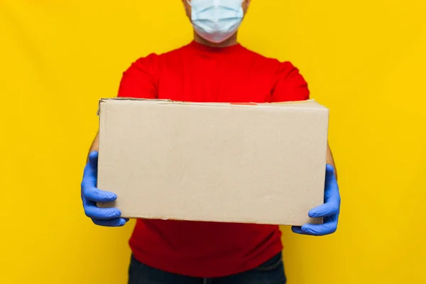 戴着医疗面罩的送货人手里拿着一个用黄色背景隔开的纸盒 网上购买检疫食品 — 图库照片