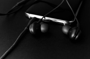 Siyah kulaklıklar, siyah cep telefonu koyu tonda siyah arka plan. Yaklaş, yumuşak odaklan