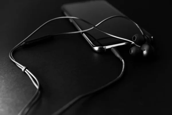 黒のヘッドフォン 黒の携帯電話暗いトーンスタイルで黒の背景に 閉じる ソフトフォーカス — ストック写真