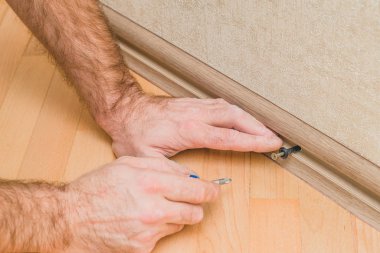 Beton ya da taş bir duvara plastik zemin kaidesi montajı ve kurulumu teknolojisi - Usta tornavida tornavidayı plastik panel tornavidasına vidalıyor