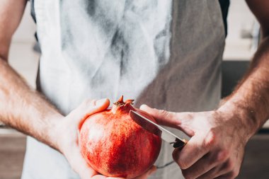 Bir adam olgun, sulu, büyük bir nar kabuğunu soyar.