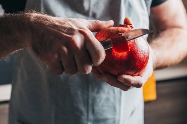 Güçlü elleri olan bir adam bir narı bıçakla keser. Yakın plan.