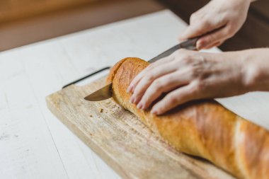 Avrupalı kadın elleri tahtadan taze ekmek kesiyor.