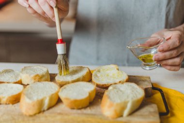 Kadınların Avrupalı elleri ekmek dilimlerini zeytinyağıyla boyar- bruschetta pişirir.