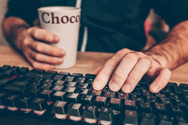 Coffee pause while working on a computer - a cup of hot coffee or cocoa in the hand of a programmer