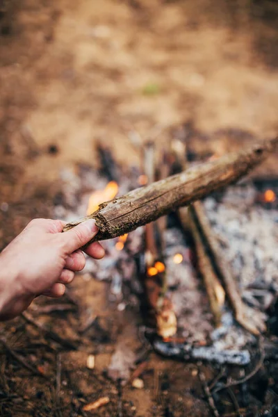 A man throws a log in a fire - tourists bask and cook dinner in the forest - overnight camping