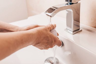 Kadın ellerini sıcak su musluğunun altında katı sabunla köpürüyor. Kişisel hijyen.