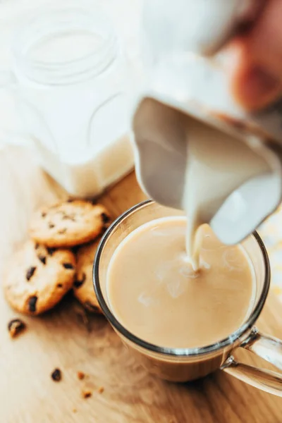 在咖啡顶部添加牛奶 一小滴牛奶会掉在杯子的表面 夹着巧克力的饼干会失去焦点 — 图库照片