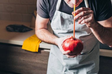 Önlüklü bir adam, nar suyundan bir kokteyl tüpü ile su içer. Sulu, olgun bir meyve. Sağlıklı bir diyet.