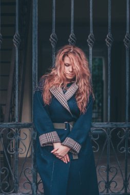Kızıl saçlı, güzel, çekici ve zarif bir kadın. Üzücü bir şekilde aşağı bakıyor.