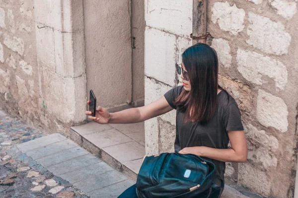 Saint-Paul-de-Vence, Provence / France - 28 Eylül 2018: Asyalı kız turist dar eski bir caddenin arka planında selfie çekiyor