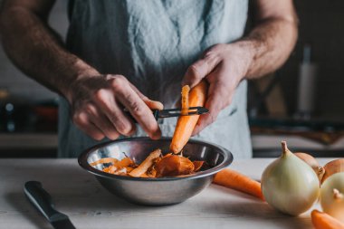 Profesyonel aşçı, özel bir bıçakla olgun turuncu havuçları temizler ve keser.