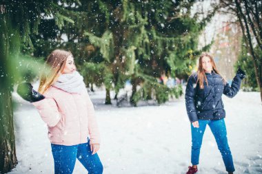 Kış eğlencesi ve sokaklarda kartopu oynayan iki genç kız arkadaş karda kar atarken eğleniyor.
