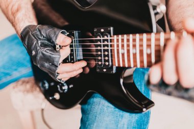 Siyah deri eldivenli bir adam siyah bir elektro gitarla hard rock çalar.