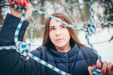 Çekici, kahverengi saçlı bir kadının yüzü rüya gibi bir şekilde bir halat ağının ötesine bakıyor. Özgürlük kavramı.