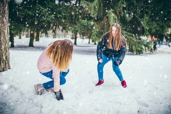 Kış eğlencesi ve sokaklarda kartopu oynayan iki genç kız arkadaş karda kar atarken eğleniyor.