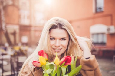 Sevilen bir adamdan hediye olarak bir buket çiçekle Avrupa görünümlü neşeli, çekici bir sarışın.