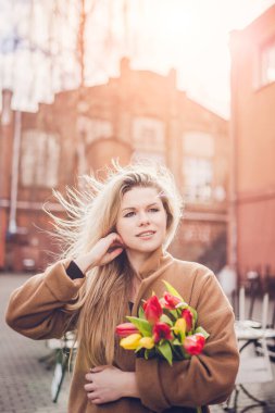 Çekici, seksi sarışın manken, rüzgarda parıldayan sarı saçları düzleştiriyor. Güneşli, rüzgarlı bahar.