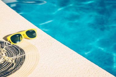 Sarı plastik güneş gözlüğü ve su kenarındaki bir taşın üzerindeki hasır şapka açık mavi - sıcak bir yaz günü