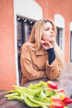 Genç ve güzel bir iş kadını. İlkbaharın başında. Şehirde çiçekler var.