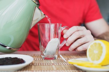 Çaydanlıktan cam bardağa kaynar su döken adam çay yapıyor - kahvaltı