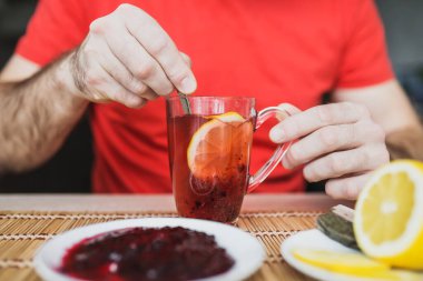 Limon ve reçeli bir fincan çaya karıştıran bir adamın elinin yakın çekimi. Soğuk algınlığı için yararlı bir vitamin içeceği.