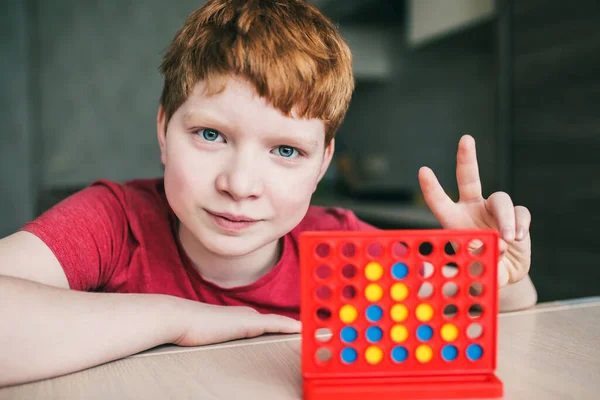 英国の外観の陽気な赤髪の少年は論理的なボードゲームで4列に勝ったと勝利の兆候を示しています 子供のレジャー — ストック写真