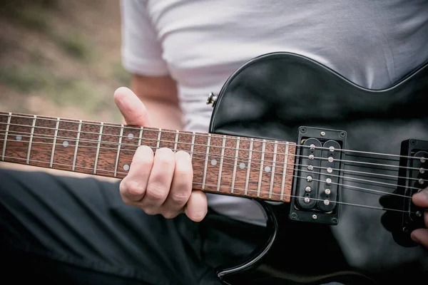 Left handed male playing a black left-handed electric guitar outside outdoors