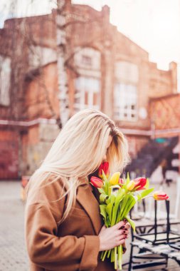 İskandinavyalı güzel sarışın kız soğuk bulutlu bir günde bir buket laleyi kucaklıyor.
