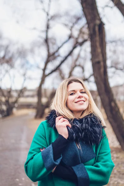 An attractive Swedish woman with a smile and pleasure wraps herself in a warm, cozy coat of green outdoors in the autumn