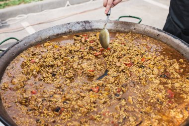 Sokakta ateşte paella pişirirken aşçı kaşıkla karıştırır.