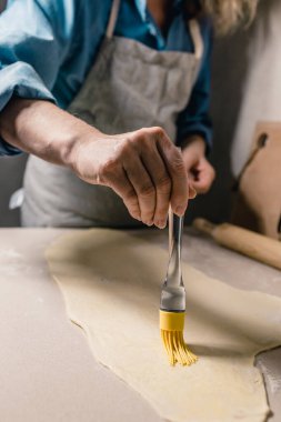 Mutfakta silikon fırçalı beyaz bir kadın tatlı olsun diye eritilmiş tereyağını tarçınlı ve şekerli koyar.