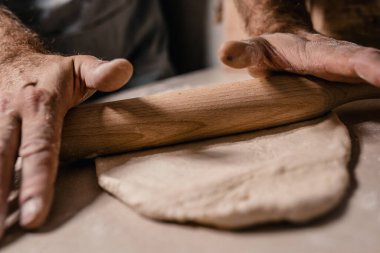Bir fırıncı elleri ahşap bir oklava ile hamuru masanın üzerinde ince bir tabaka haline getirir.