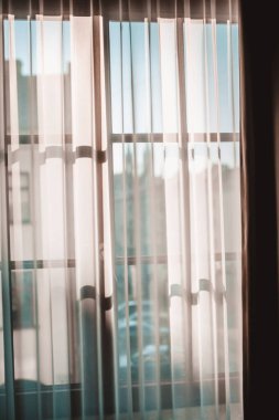 Sabah güneşi penceredeki şeffaf perdelerin arasından geçiyor.