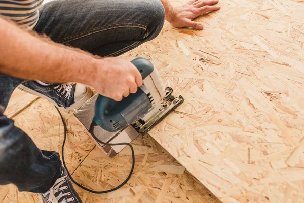 Usta bitirici bir yapboz kullanarak bir parça OSB 'yi testereyle kesiyor.