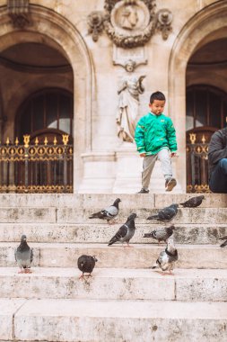 Paris, Fransa - 2 Ekim 2019: Yeşil ceketli Asyalı çocuk Grand Opera 'nın merdivenlerinde güvercin kovalıyor