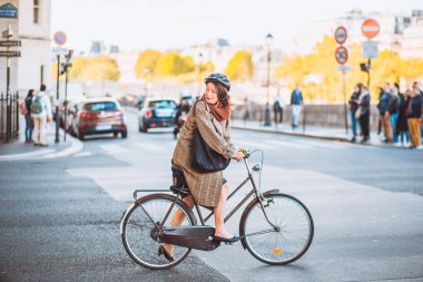 Paris, Fransa - 02 Ekim 2019: Şehirde bisiklet süren yağmurluk ve etekli genç çekici kadın