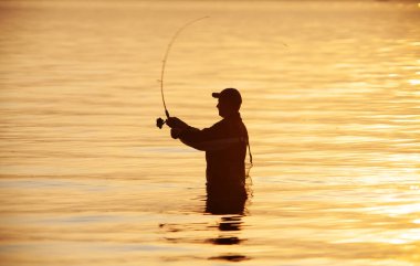 Gün batımında balık tutan bir adamın tanınmaz bir silueti.