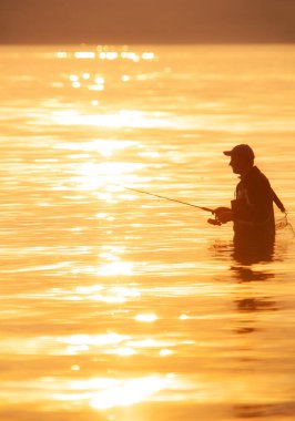 Gün batımında balık tutan bir adamın tanınmaz bir silueti.