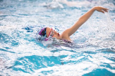 Yüzme eğitiminde havuzda yüzen küçük kız.