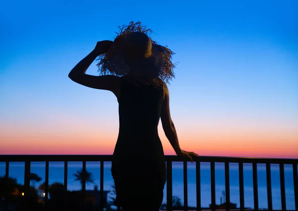 Silhouette of young woman looks at the sea at sunset in a tropical resort
