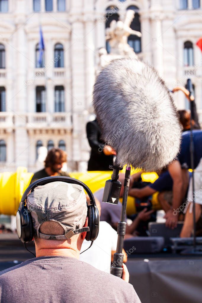 Behind the scene. Sound recorder with microphone, boom mic and headphones filming movie scene on outdoor location 