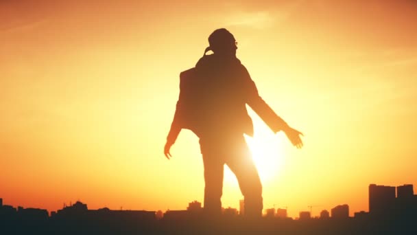 Silueta de un hombre con una mochila contra la puesta de sol del cielo brillante — Vídeos de Stock
