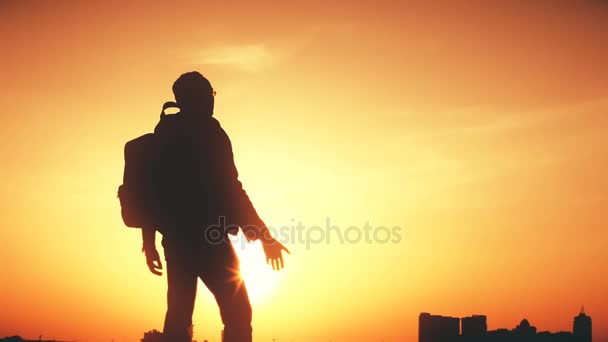 Silueta de un hombre con una mochila contra la puesta de sol del cielo brillante — Vídeos de Stock