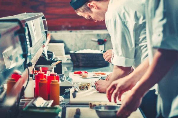 Zwei junge Köche in weißen Uniformen bereiten Sushi zu — Stockfoto