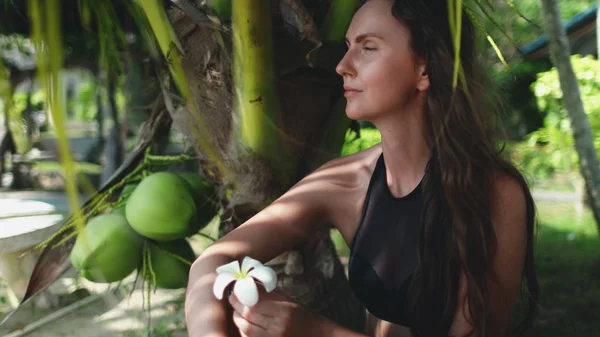 Genç, kaygısız kadın palmiye yaprağının altında oturuyor. — Stok fotoğraf