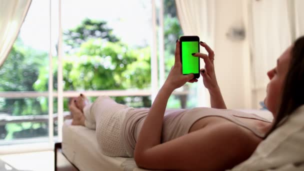 Женщина лежит на кровати со смартфоном альфа-канал — стоковое видео