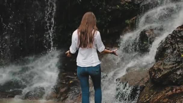 Turista mujer levantar las manos a salpicaduras cascada — Vídeo de stock