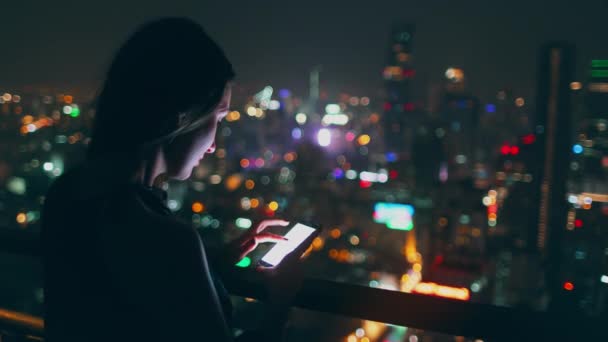 Belle fille parcourir smartphone nuit skyline toit — Video