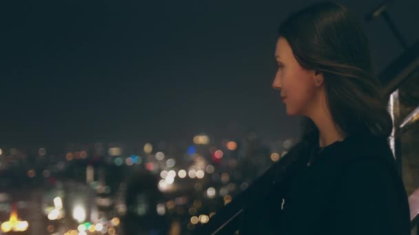 Mujer bonita mirar hacia abajo noche paisaje urbano azotea — Vídeos de Stock